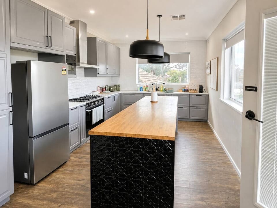 Generous open-plan kitchen with large island bench, pendant lighting and stainless appliances — plenty of room for everyone to gather and prep meals.
