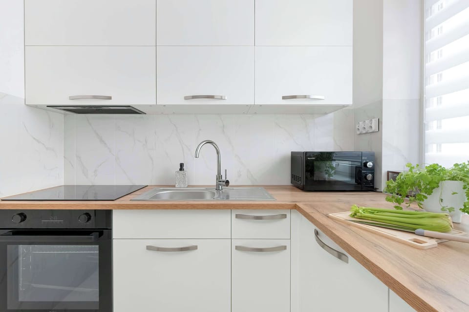 A modern kitchen is equipped with white cabinets, built-in appliances, and wooden countertops. The simple design combines practicality with contemporary style.