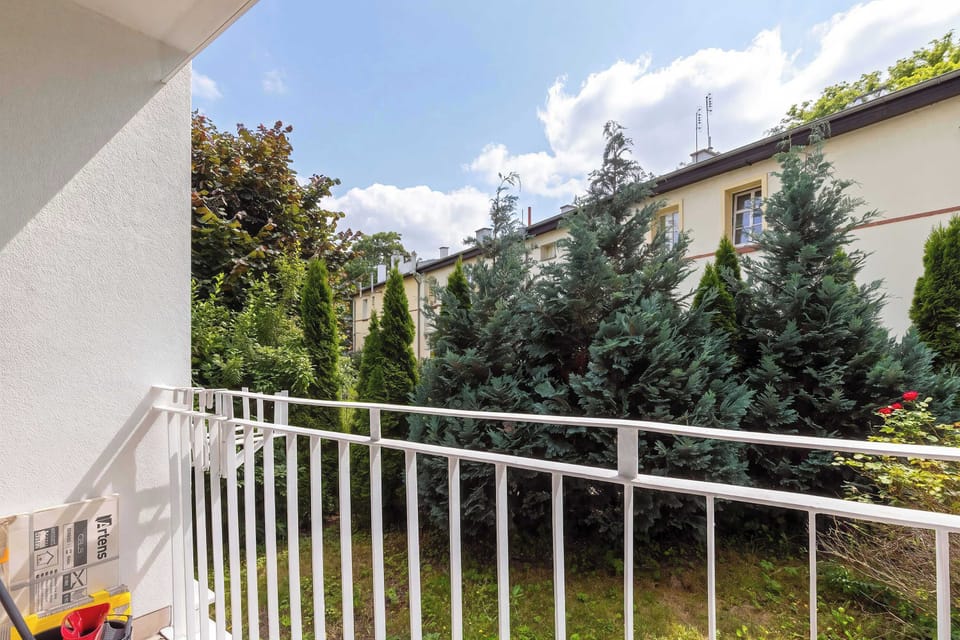 A private balcony overlooks mature trees and neighboring buildings, offering a peaceful outdoor retreat. The railing provides an unobstructed view of the surrounding greenery.