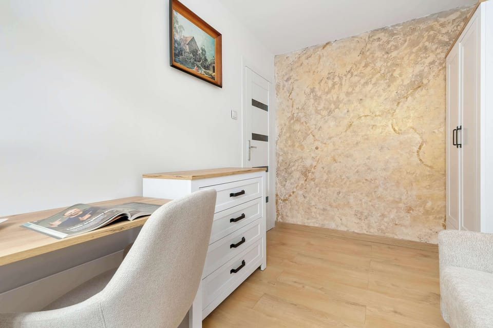 A bedroom corner features a writing desk, upholstered chair, and textured accent wall. The room offers a quiet and comfortable place to work.