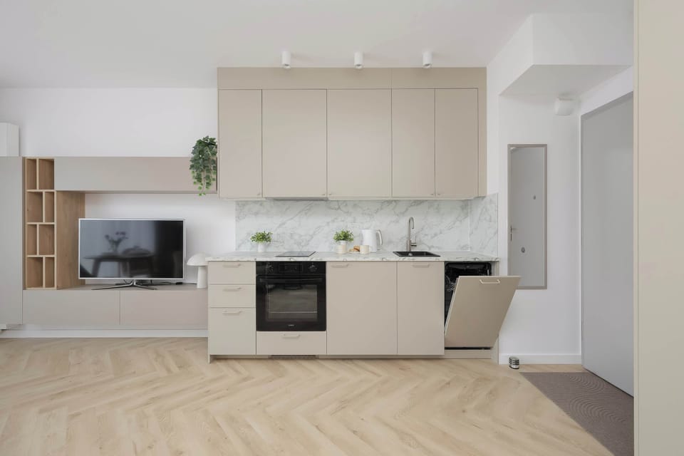 A modern kitchenette with light cabinets, a built-in oven, and a dining area nearby.