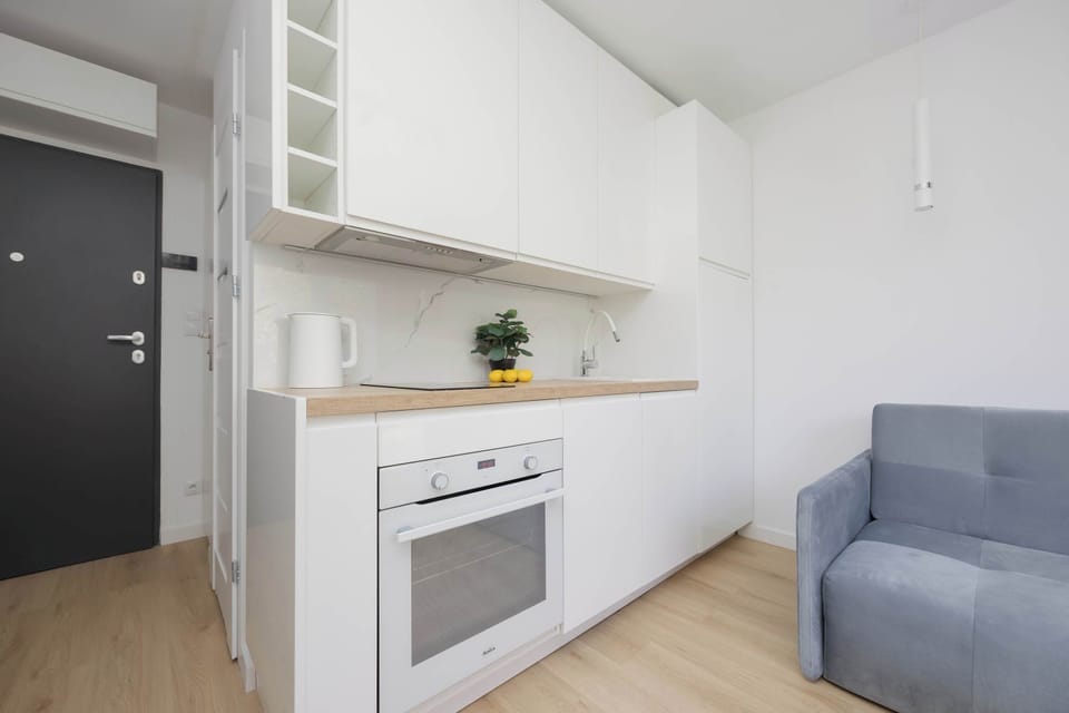Functional kitchenette with built-in oven, induction hob, refrigerator, and white cabinetry.