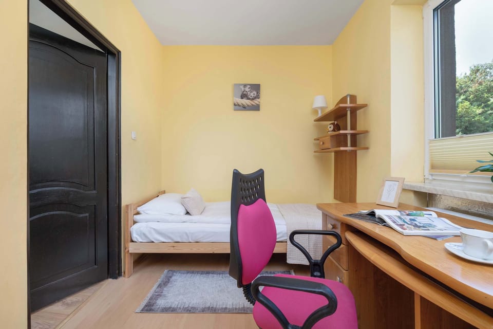 Bright bedroom with a single bed, desk, chair, and large window.