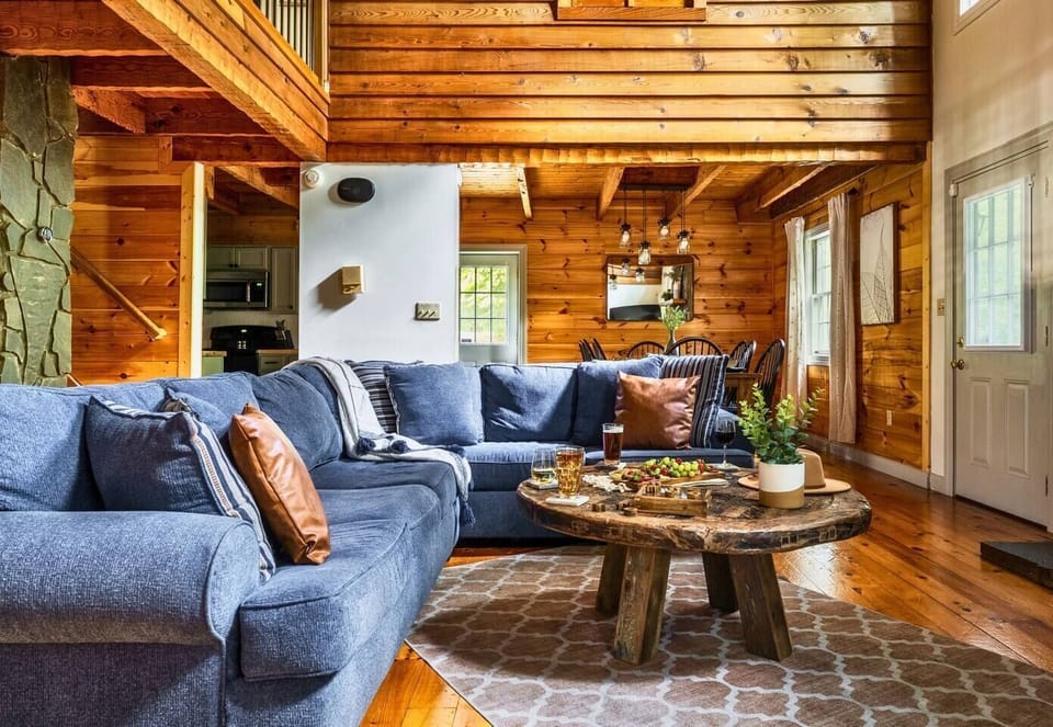 Relax in this spacious and cozy living room, featuring plush seating, a warm stone fireplace, and charming rustic cabin vibes.