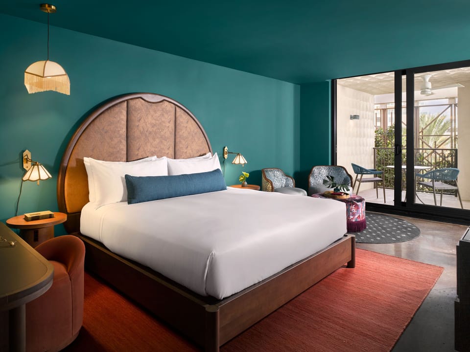 King bed with plush pillows and a dresser in the bedroom, with access to the private balcony beyond