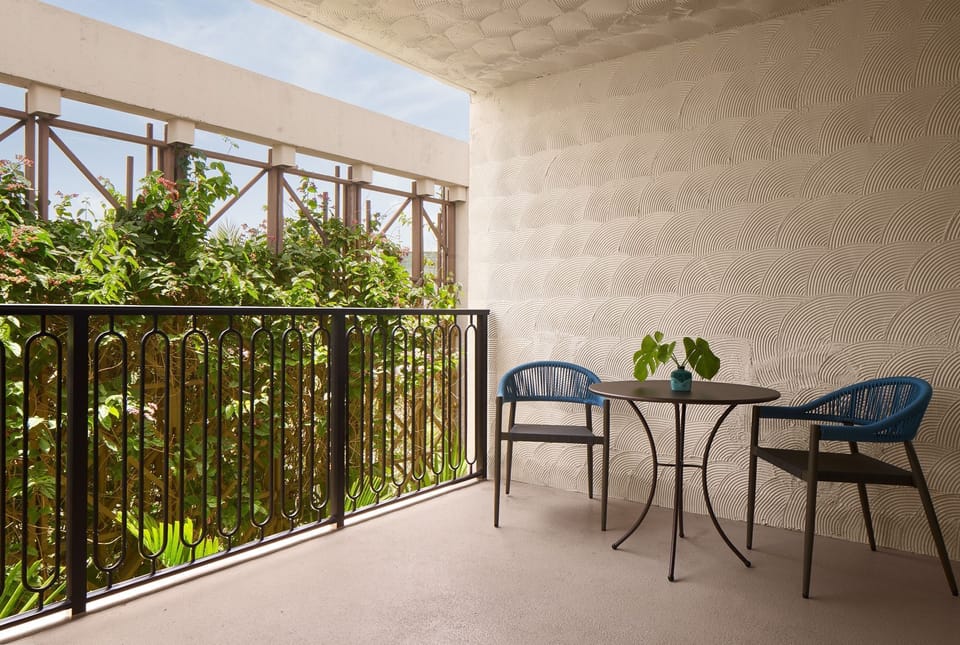 Black wrought iron railing on the private balcony, with two blue woven chairs around a small table and lush greenery beyond