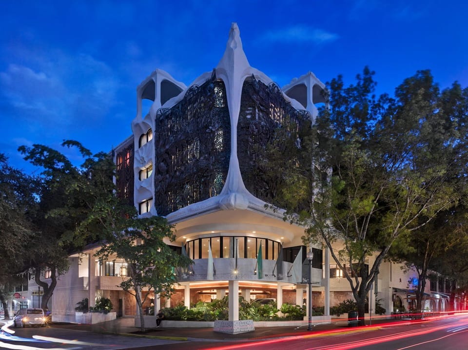 A striking facade with organic shapes and intricate carved details merges with lush surroundings at twilight