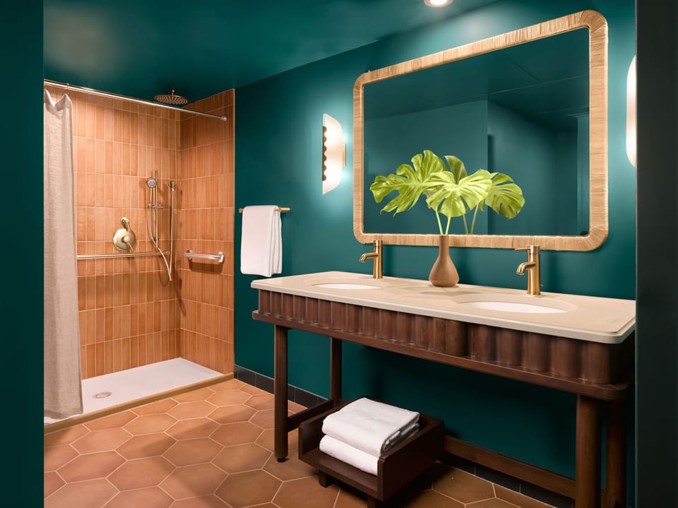 Accessible roll-in shower with terracotta tile, double vanity with brushed gold fixtures, and a gold-framed mirror