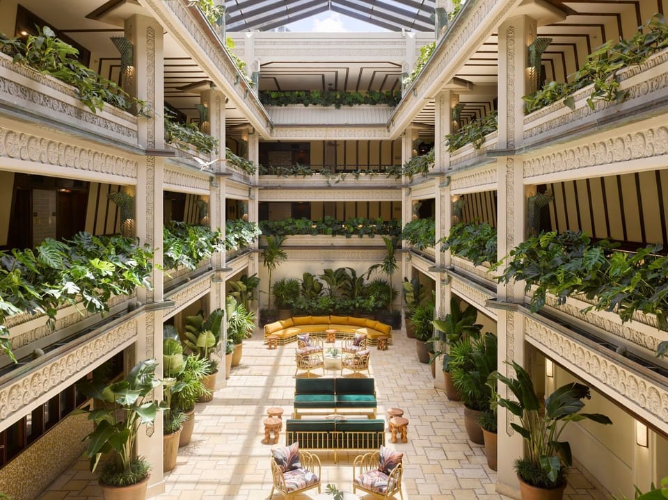 Lush greenery fills the atrium, where intricately carved columns rise around plush seating areas