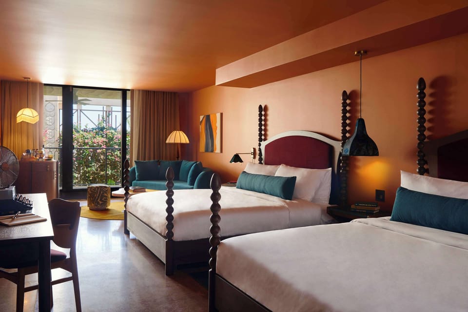 Wide view of both king beds, teal sofa, and the balcony beyond — the full room layout in warm terracotta tones