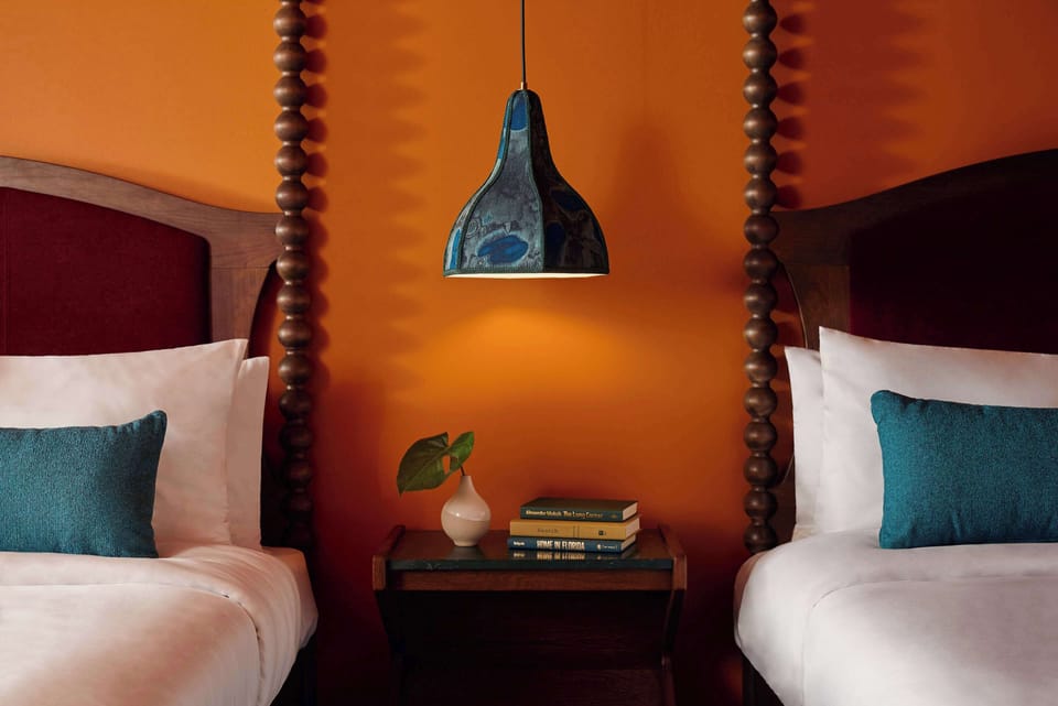 Between two spool-post beds, a dark wood nightstand with stacked books and an iridescent blue pendant lamp overhead