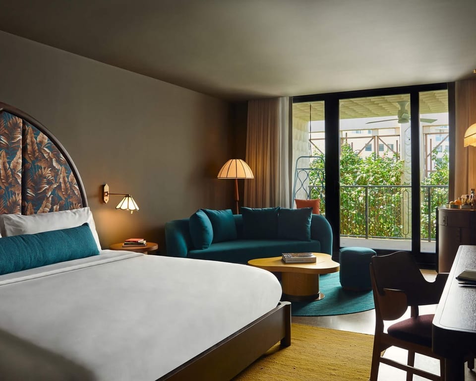 King bed with a botanical-print arch headboard, teal velvet sofa, and floor-to-ceiling balcony door overlooking the garden
