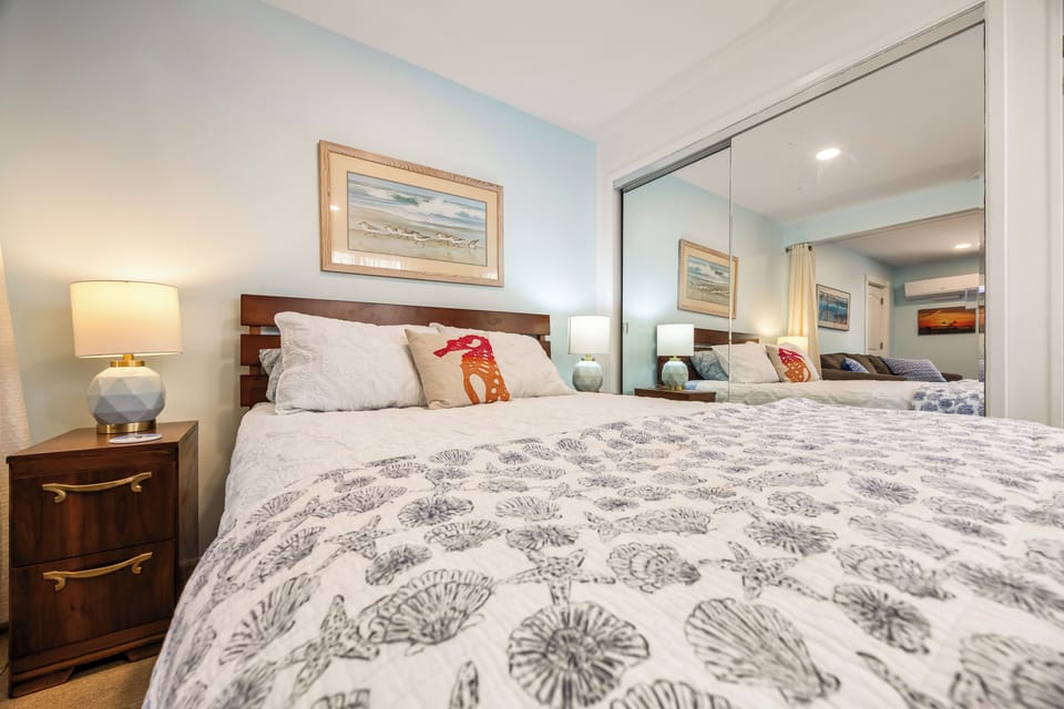Relaxing bedroom featuring a Queen bed with coastal seashell bedding, bedside tables, and full mirrored closet doors.