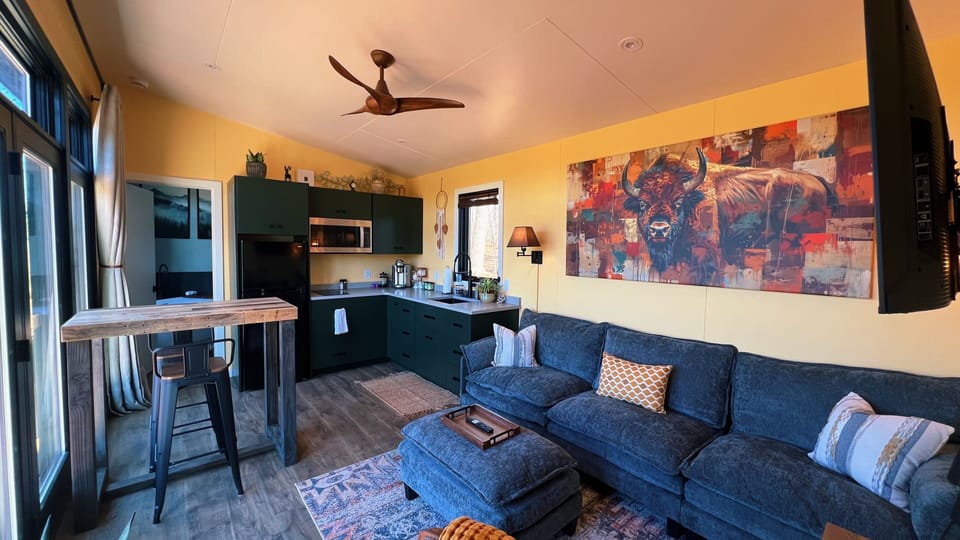 Bright open-plan lounge with green kitchen, bar table, and plush sofa