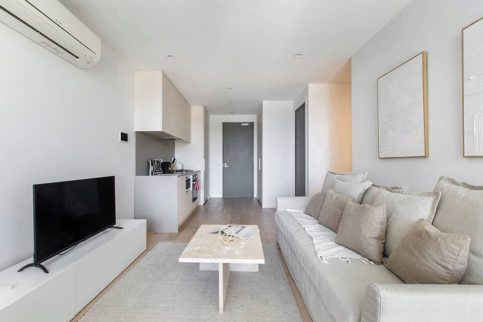 This living area is beautifully laid out in white/cream colours, with a featured stone coffee table, cream rug and couch, increasing the flow of natural light through the apartment

