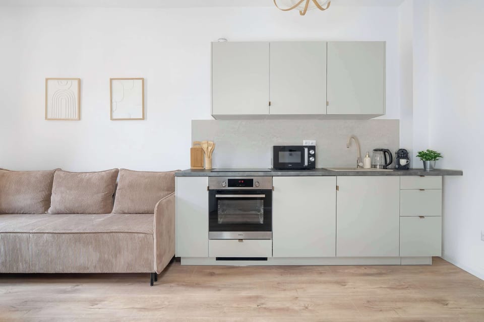A straight-on view showcases the light grey kitchen cabinetry and built-in appliances. The living room sofa stands on the left.