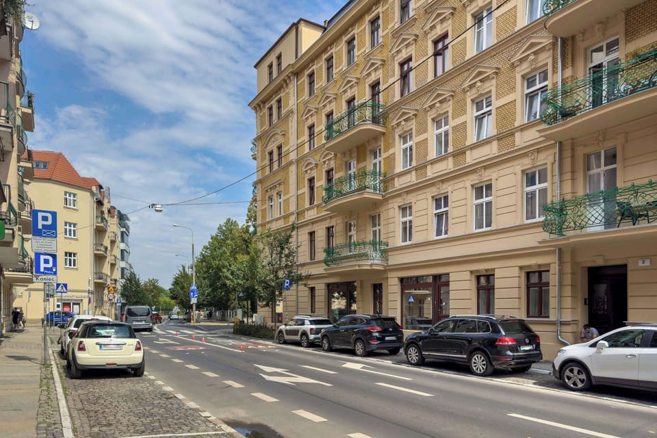 A street-level perspective showcases the classic grand facade of the historic residential building under a bright blue sky.