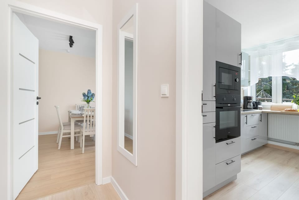 A hallway connecting the bedrooms with the living area and kitchen. Bright walls and mirrored wardrobe doors make the apartment feel more spacious.
