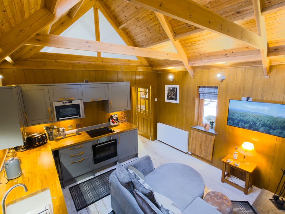 The kitchen sits under an open timber roof with the beams on show. Everything you need to cook properly, with the sofa only a few steps away.