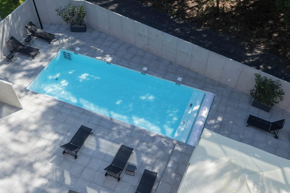 Aerial view of a modern outdoor swimming pool surrounded by trees, greenery and a paved poolside area.