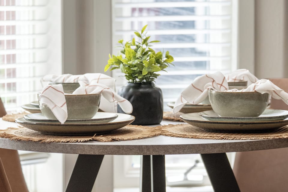 Settle in for a relaxed meal at your thoughtfully set table, complete with modern dinnerware and fresh greenery. Natural light pours through the windows, creating a warm and inviting space for your morning coffee or evening dining.