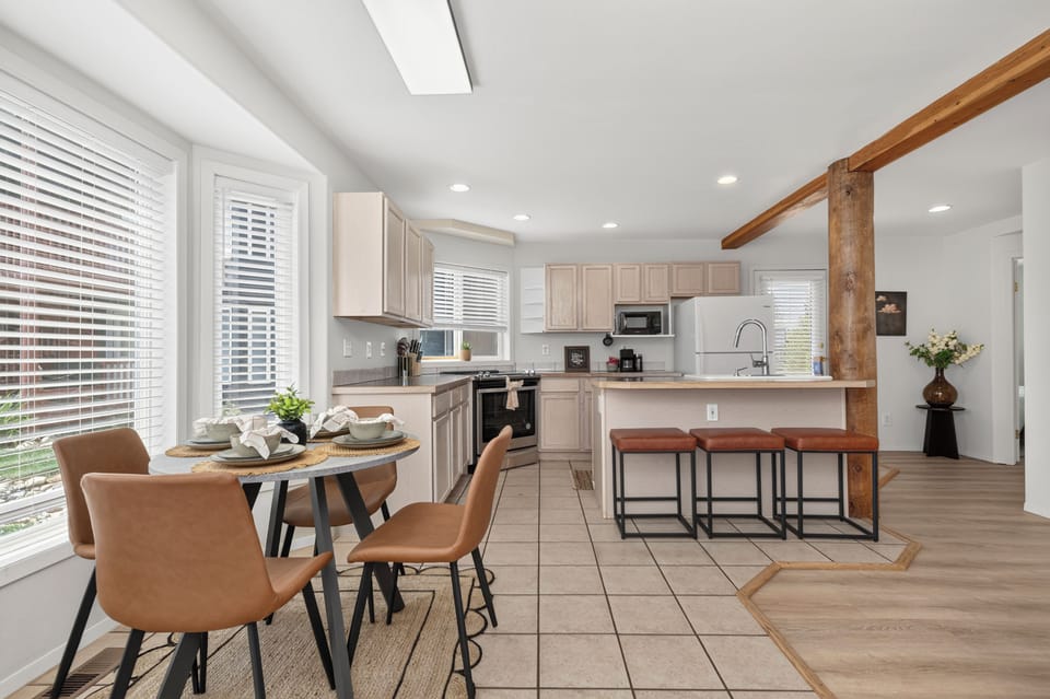 Gather around your cozy dining table or pull up a stool at the breakfast bar in this bright, airy kitchen—where sunlight streams through generous windows and that rustic wooden beam adds a touch of character overhead.