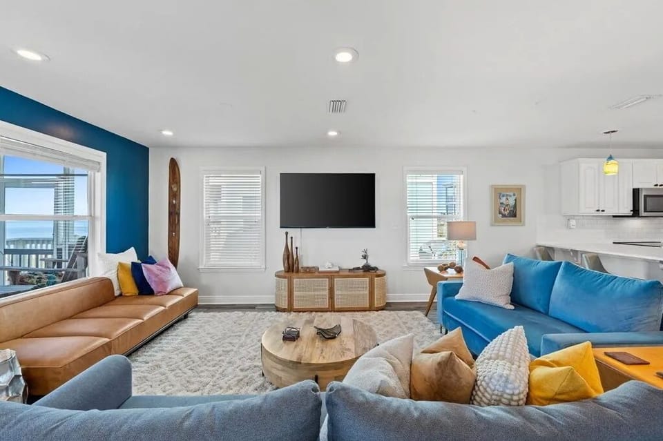 Settle into this bright, open living space where pops of ocean blue and warm textures invite you to relax. Large windows frame natural light, and the coastal vibe makes unwinding effortless.