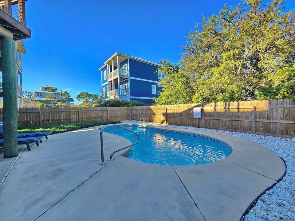 Private pool oasis with crystal-clear water surrounded by coastal charm and vibrant blue skies.