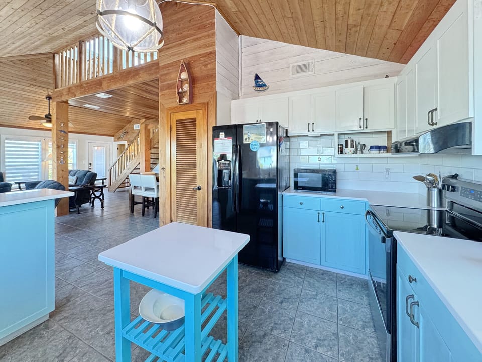 Your bright, coastal-style kitchen features turquoise cabinets, modern appliances, and nautical charm, perfect for preparing meals in your beach getaway.