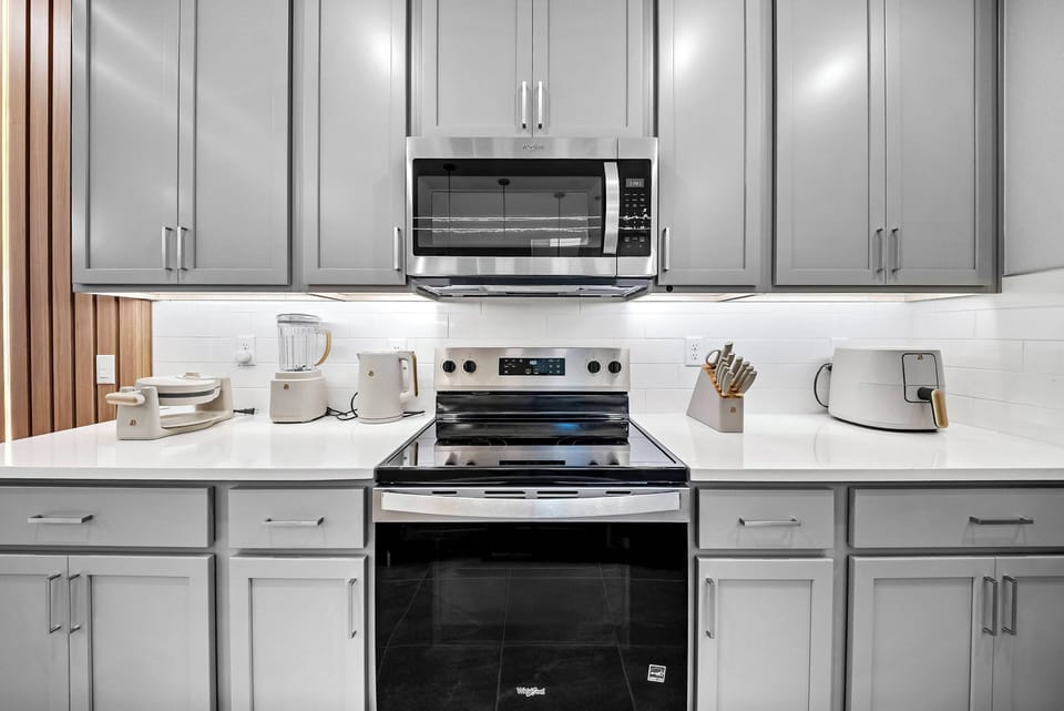 Welcome to this stylish kitchen with sleek gray cabinetry and bright countertops. Modern stainless steel appliances, including a microwave and stove, inspire culinary creativity while ensuring practicality for your cooking needs.