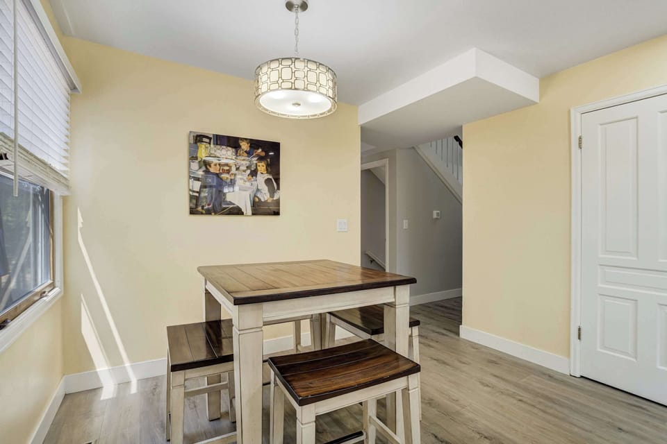 The breakfast nook keeps mornings casual, with wooden stools pulled up to a tall table and framed artwork on the wall alongside it. Light from the side window fills the space well before the rest of the house has woken up