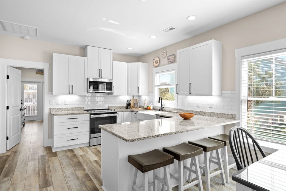 Your home-away-from-home features a bright, modern kitchen with gleaming white cabinetry, granite countertops, and a spacious island perfect for gathering over morning coffee or meal prep.