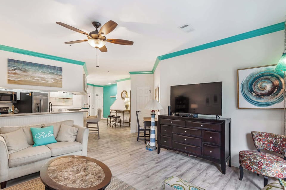 Coastal charm meets comfort at 35 Ocean Breeze! Teal crown molding, ocean artwork, and a "Relax" pillow set the beachy vibe. Open layout connects living room, kitchen, and dining area with wood-look floors.