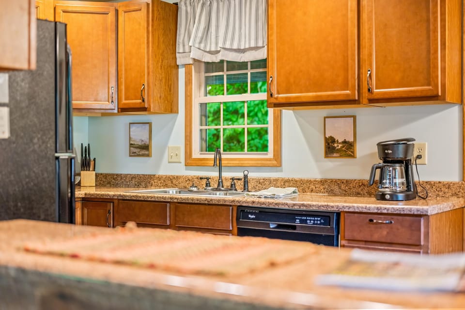 Kitchen countertop with granite finish, double stainless steel sink, black dishwasher, and black coffee maker beneath wood cabinets.