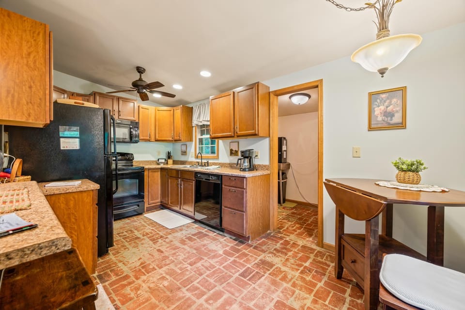 Brick-patterned tile covers the kitchen floor beneath honey-toned cabinets and black appliances with recessed ceiling lights.
