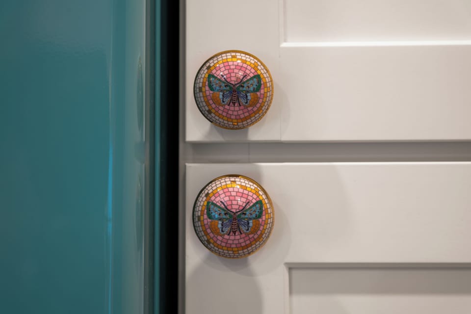 Colorful butterfly knobs add a playful boutique touch to crisp cabinetry
