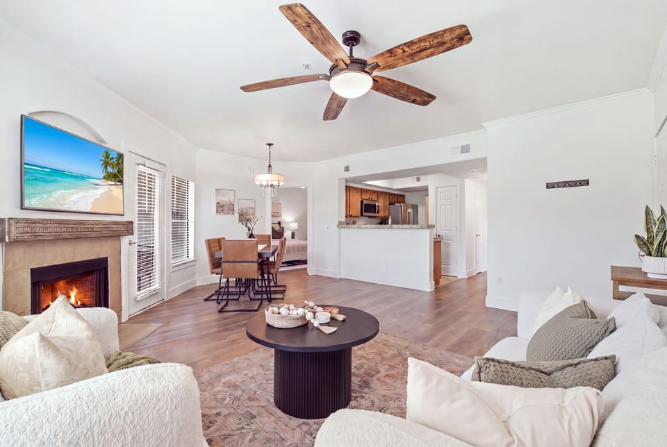 The living room's gas fireplace sets a cozy glow beside a mounted smart TV, with an open flow into the kitchen and dining area for easy gathering.