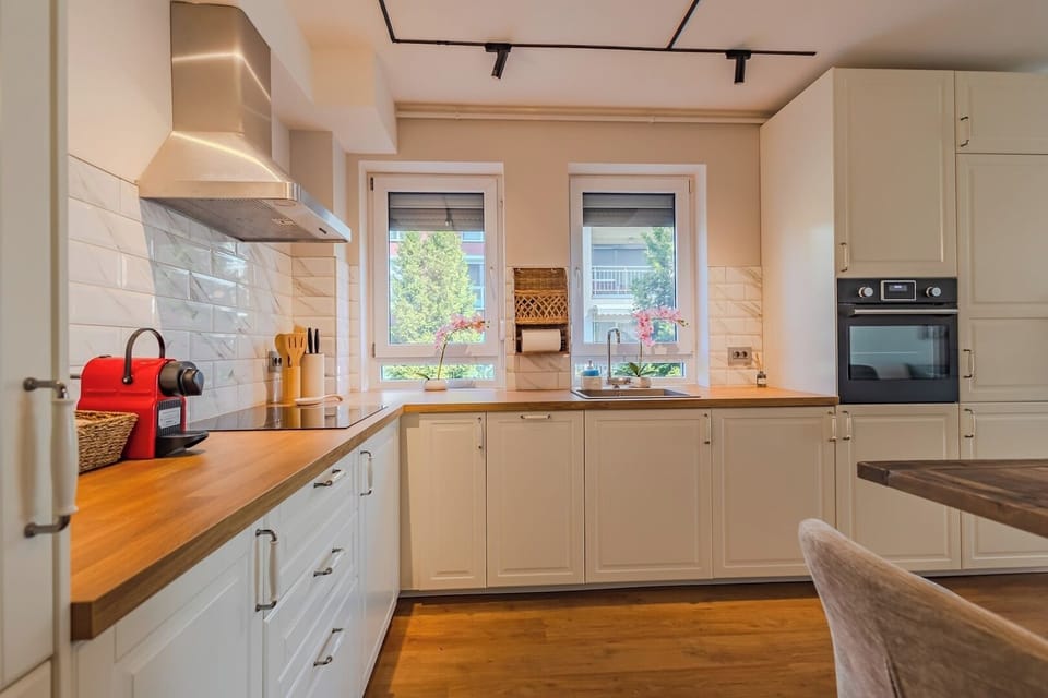 Kitchen with natural light from two windows, white cabinetry, solid wood worktop, 4-ring induction hob, electric oven, dishwasher and mixer. Fully equipped for self-catering stays in Brasov, sleeps up to 4.