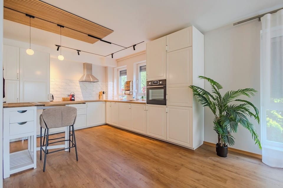 Generous L-shaped kitchen with white cabinetry, solid wood worktop, electric oven, extractor hood and 4-ring induction hob. Dishwasher included. Track lighting and bar stools. White Feather by Bianca, Brasov.