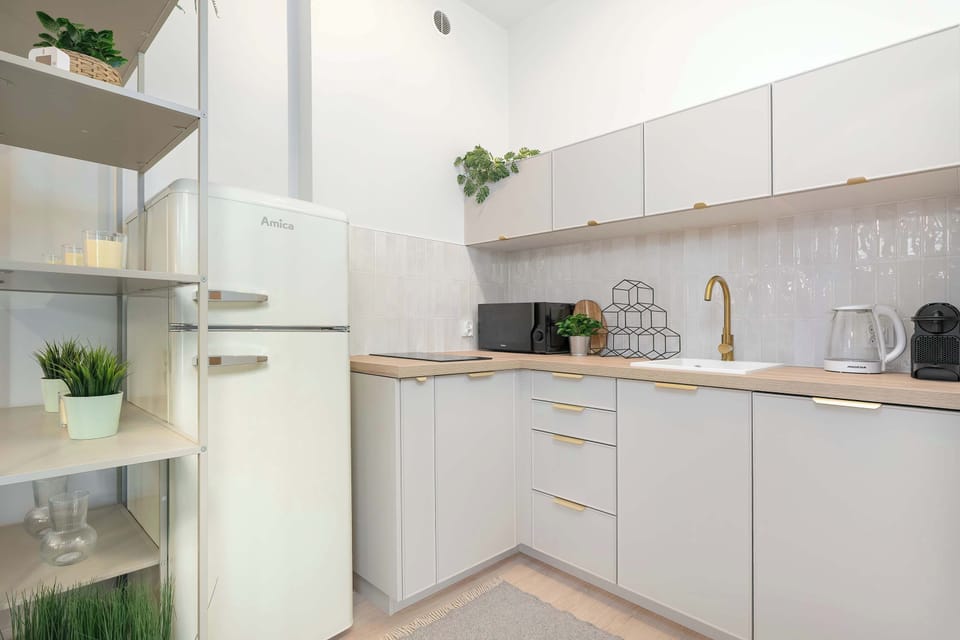 Modern kitchenette with white cabinets, light countertops, a sink, cooking area and shelves decorated with plants and other accessories.