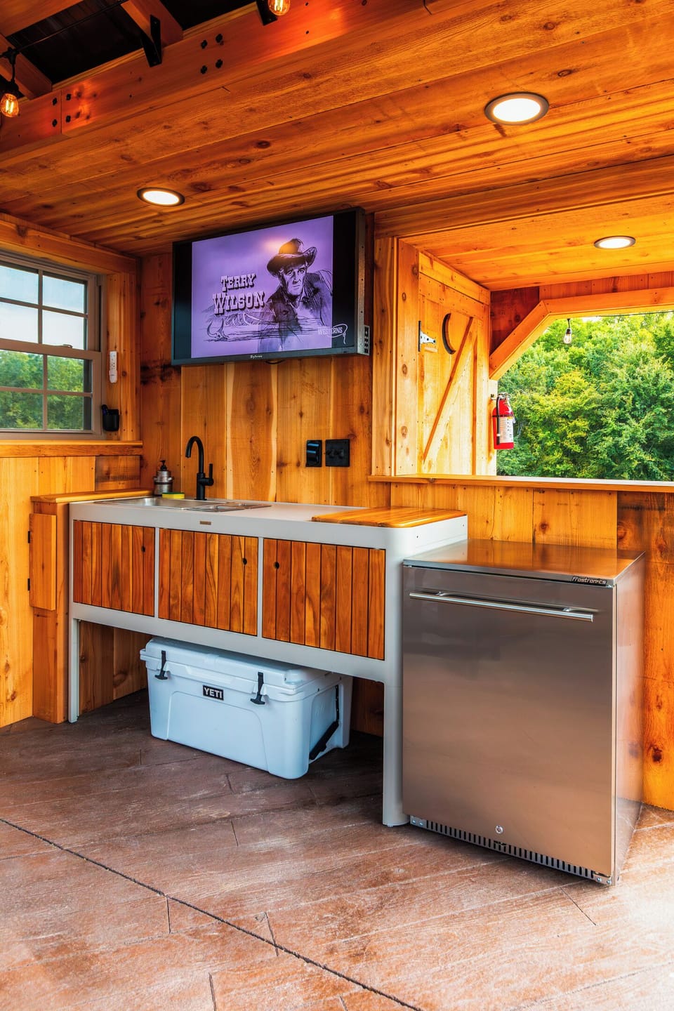 Outdoor kitchen setup with sink, beverage refrigerator, cooler space, and covered prep area.