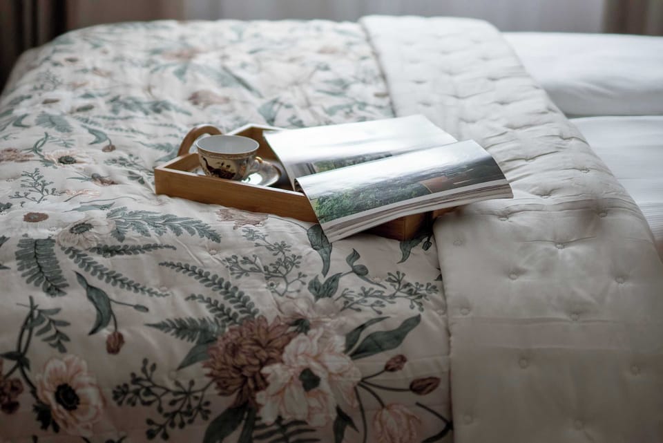 A detailed shot of a bed styled with a floral quilt and a wooden breakfast tray carrying a magazine. Crisp white pillows add a cozy, inviting feel to the bedroom space.