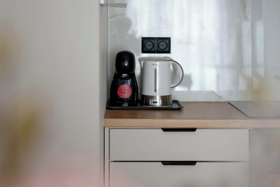 A close-up of a wooden countertop space featuring an electric kettle and coffee capsule machine. Sleek white drawers beneath offer clean, modern storage solutions.