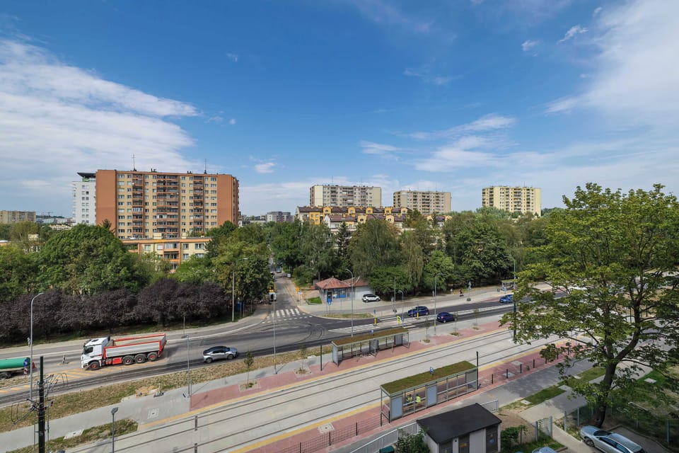 A balcony overlooking a road, greenery, and surrounding residential buildings. The elevated view provides a pleasant perspective of the neighborhood.