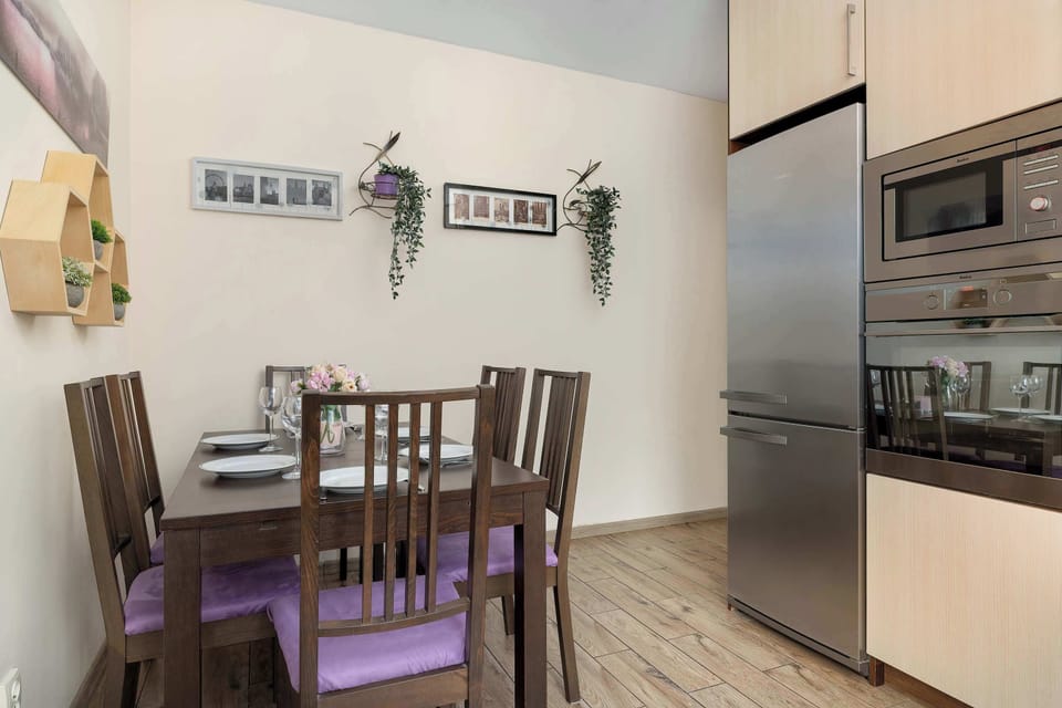 A dining area with a wooden table and chairs positioned next to the kitchen. The refrigerator, oven, and cabinets are visible in the background.