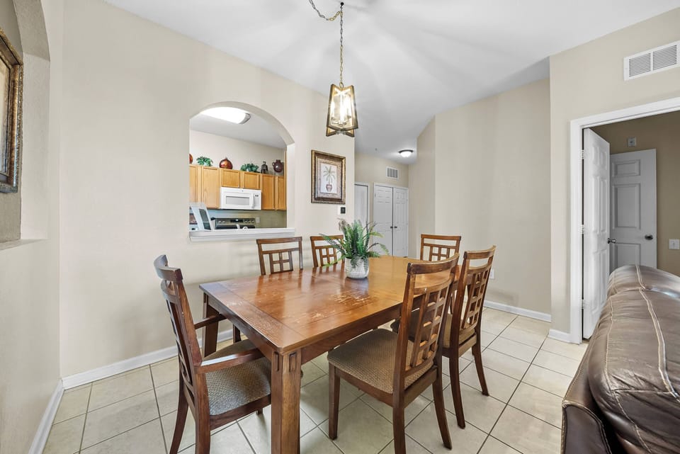 Join us at the cozy wooden dining table, bathed in natural light from the archway, creating an inviting ambiance. The warm chair tones harmonize with the earthy tile floor, making it ideal for shared meals and laughter.