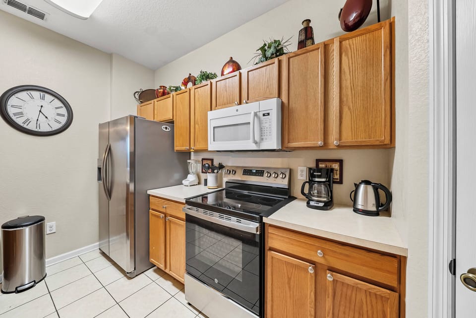Welcome to a beautifully designed kitchen featuring warm wooden cabinetry and stainless steel appliances. The bright tile floor creates an airy atmosphere, perfect for meal prep or casual dining, complemented by a charming clock.