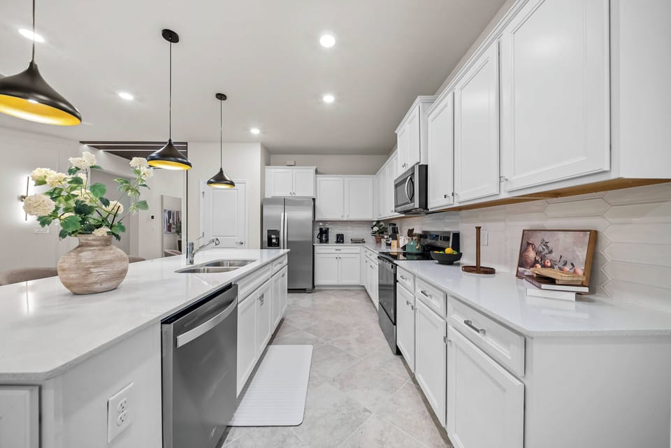 Welcome to this bright kitchen, featuring sleek white cabinetry and beautiful marble countertops that create an airy feel. Modern pendant lights above the island add warmth, while stainless steel appliances make cooking a breeze.