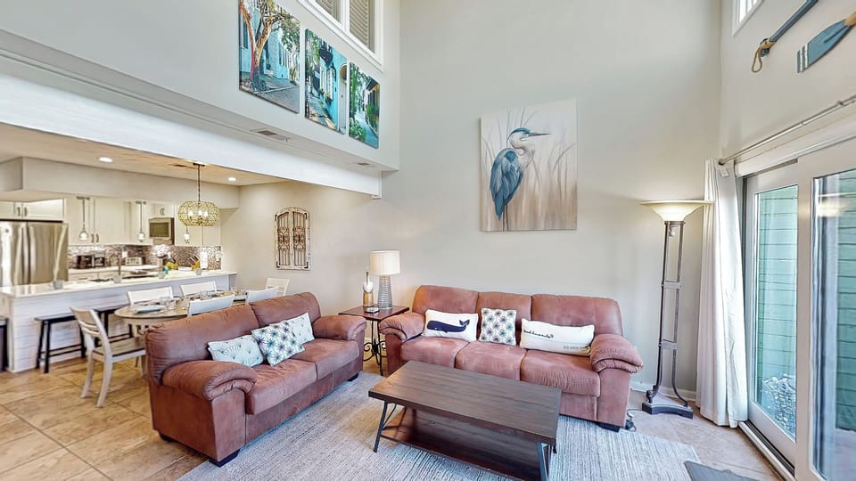 Relax in your bright, open living space with soaring ceilings, plush seating, and soft natural light. The coastal artwork adds a peaceful touch while you unwind after a day of exploring.