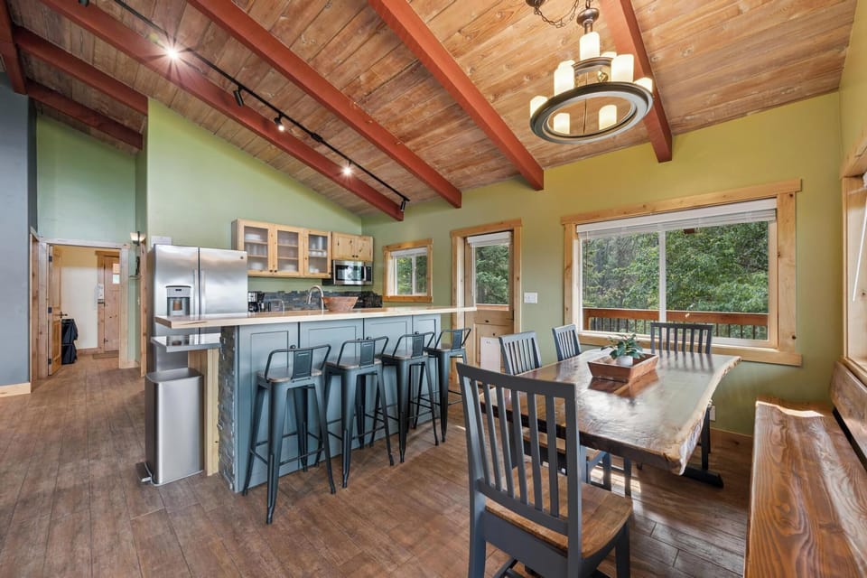 Gather around the open kitchen and dining area, where vaulted wood-beamed ceilings and forest views through large windows create your ideal mountain retreat.